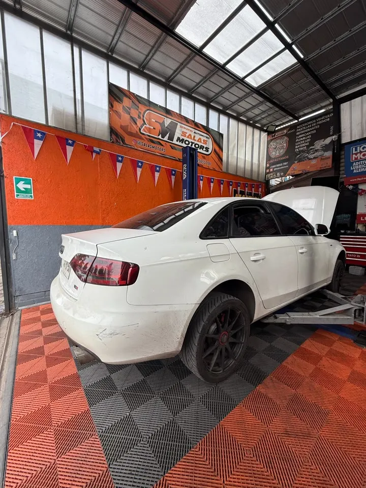 Audi A4 blanco con el capó abierto sobre el piso naranja y negro del taller