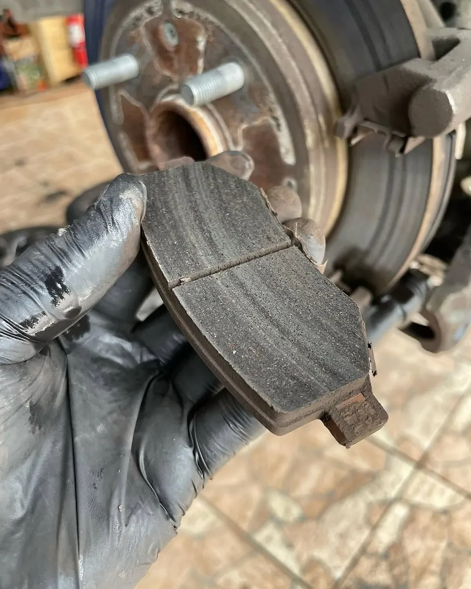 Mano con guante muestra una pastilla de freno gastada