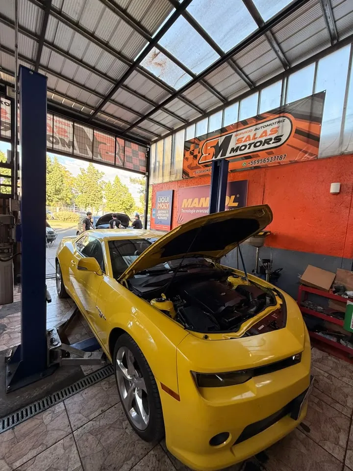 Chevrolet Camaro amarillo con el capó abierto en un elevador del taller