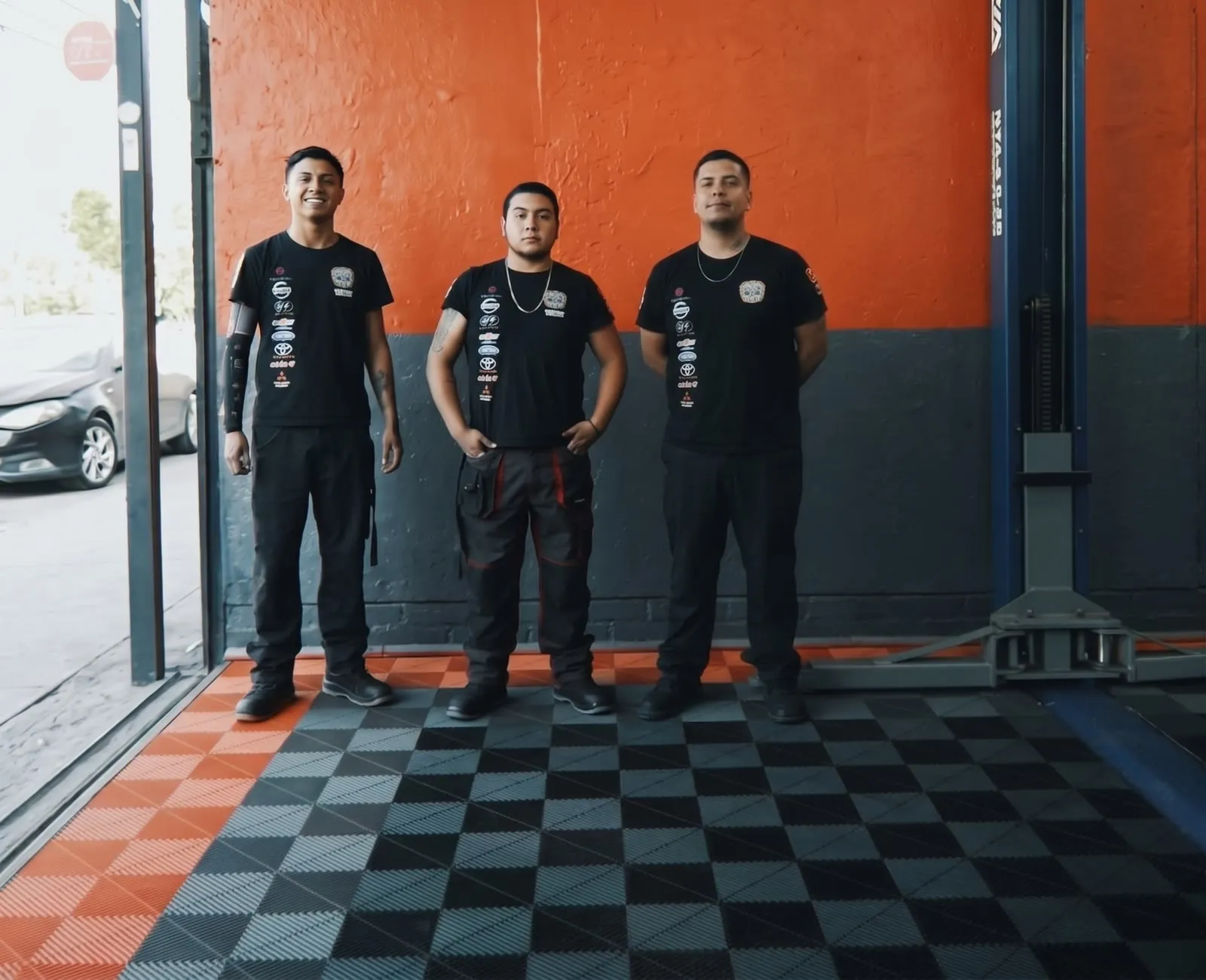 Matías Pavez Osorio, Matías Salas Flores y Fernando Muñoz Araos, de pie en el taller frente a la pared naranja