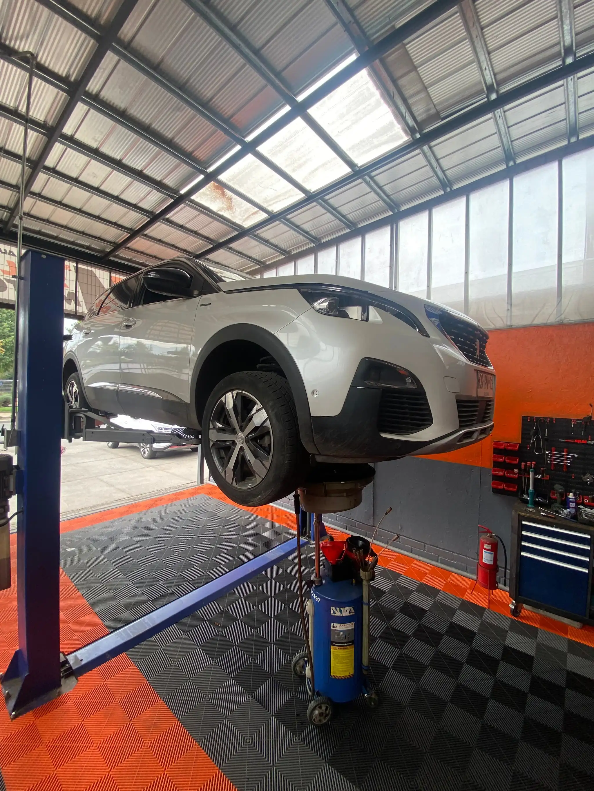 Peugeot 3008 plateado levantado en un elevador del taller SalasMotors, con herramientas y pared naranja al fondo