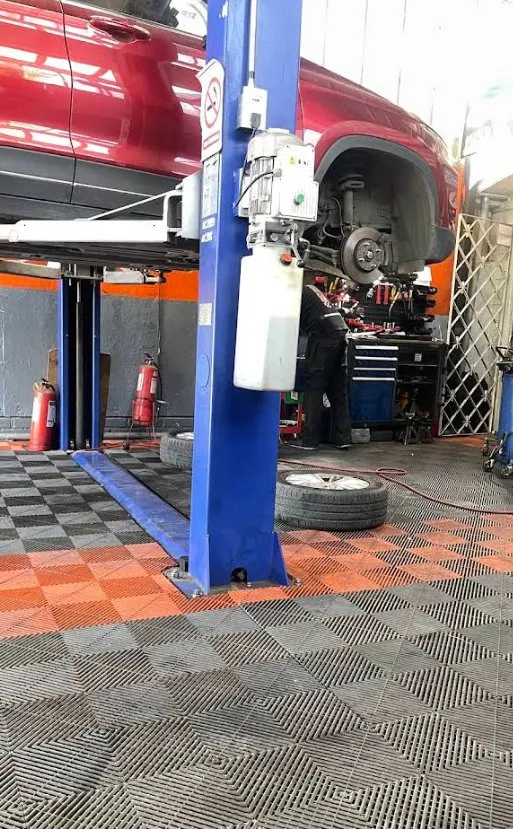 Auto rojo en el elevador del taller, con la rueda delantera desmontada