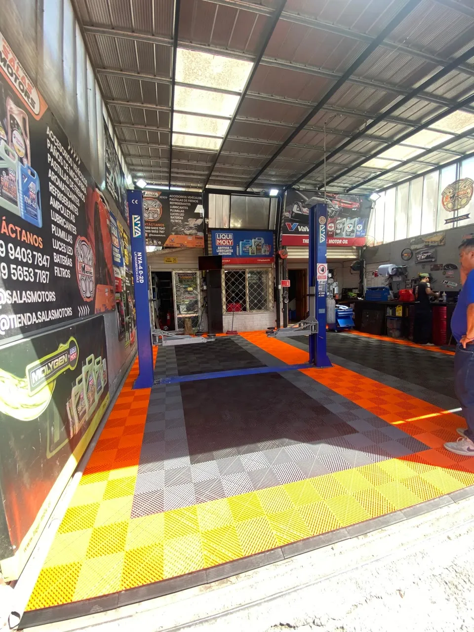 Interior de SalasMotors visto desde la entrada: piso naranja y negro, dos elevadores y la tienda al fondo
