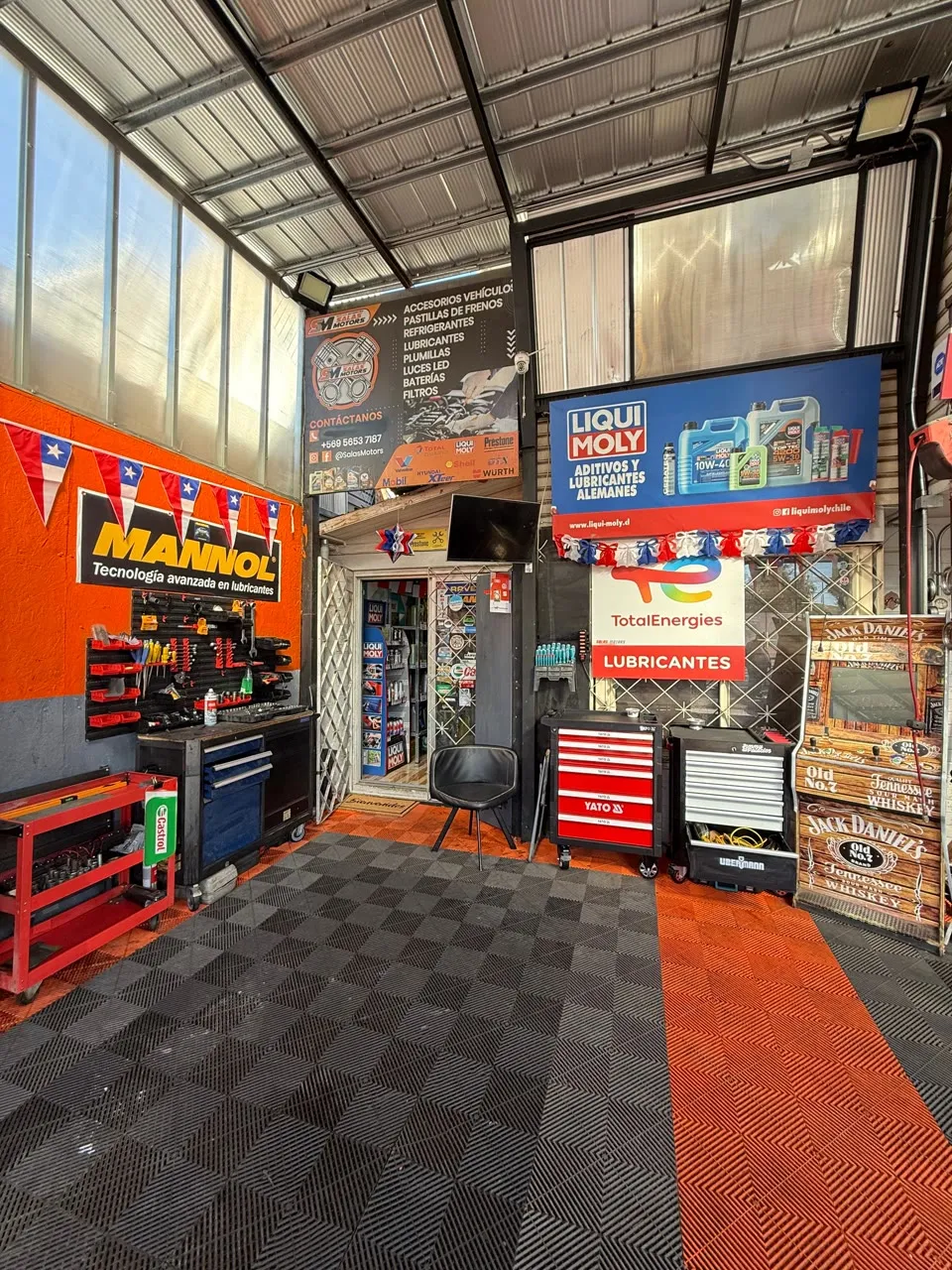 Rincón de insumos del taller con letreros de Mannol, Liqui Moly y TotalEnergies, carros de herramientas y la tienda