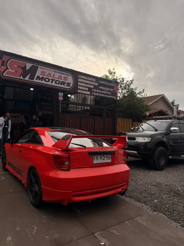 Toyota Celica rojo con alerón, estacionado frente al letrero de SalasMotors